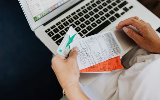 Close-up of hands holding receipts and a bank card in front of a laptop, representing online shopping and e-commerce.