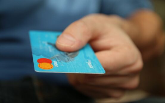 A close-up shot of a hand offering a blue debit card for payment.